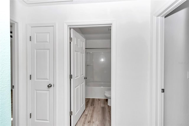 bathroom with hardwood / wood-style floors,  shower combination, and toilet