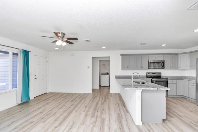 kitchen featuring sink, gray cabinets, light stone counters, stainless steel appliances, and washer / dryer