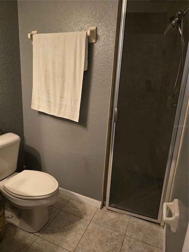 bathroom with tile patterned flooring, toilet, and a shower with door