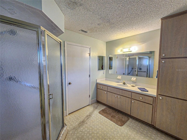 bathroom with a textured ceiling, vanity, and a shower with shower door