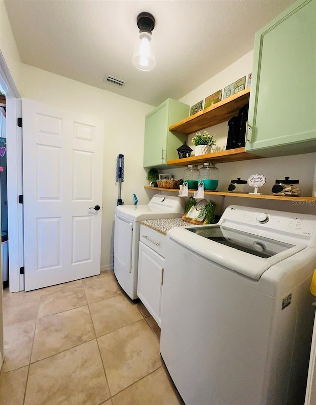 clothes washing area featuring cabinets, light tile patterned floors, and washing machine and dryer