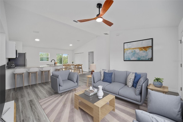 living room with light hardwood / wood-style floors, ceiling fan, lofted ceiling, and sink