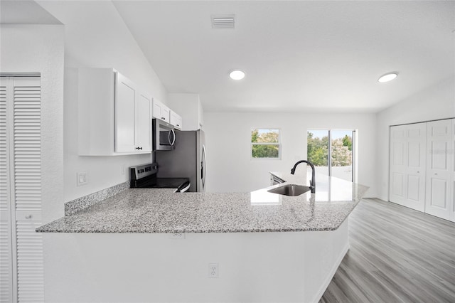 kitchen featuring stove, kitchen peninsula, sink, light stone countertops, and white cabinetry