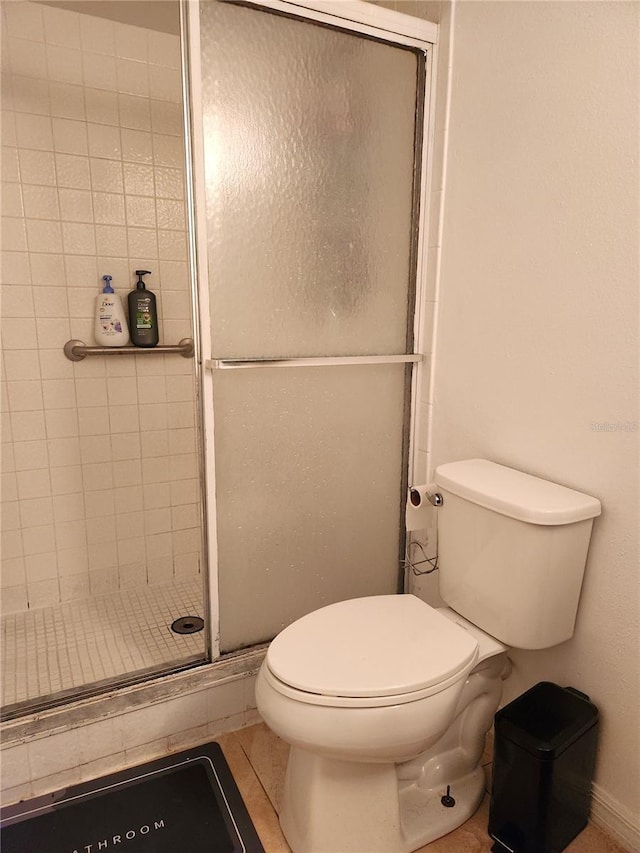 bathroom with tile patterned floors, toilet, and a shower with shower door