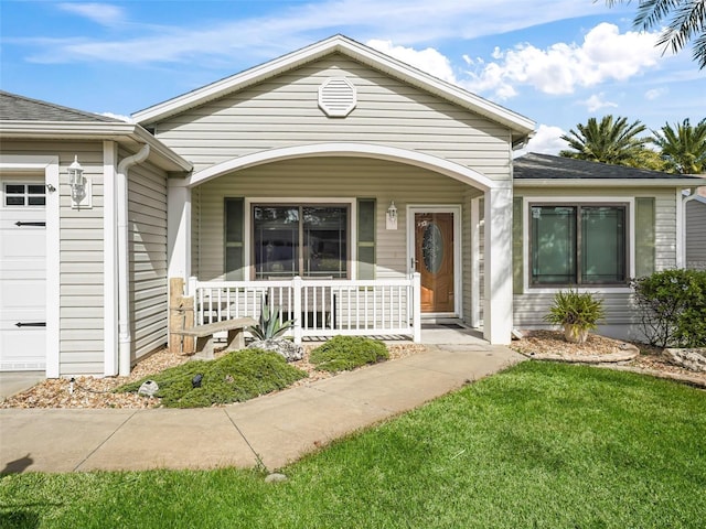 view of exterior entry featuring covered porch and a lawn