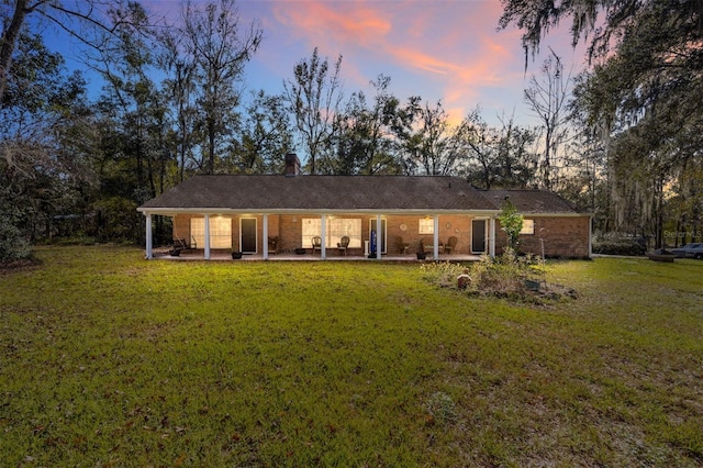 back house at dusk featuring a yard and a patio area