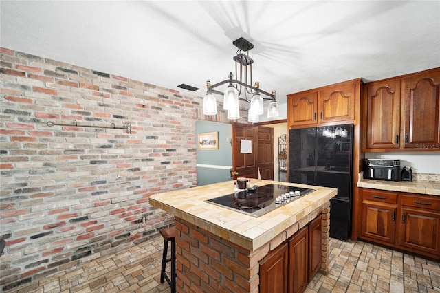 kitchen with tile counters, a center island, brick wall, decorative light fixtures, and black appliances