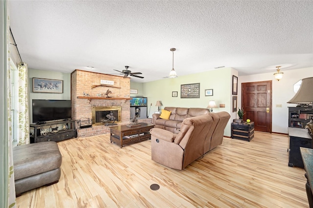 living room featuring a brick fireplace, a textured ceiling, light hardwood / wood-style flooring, and ceiling fan