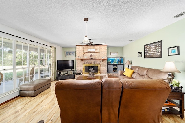 living room featuring ceiling fan, a fireplace, wood-type flooring, and a textured ceiling