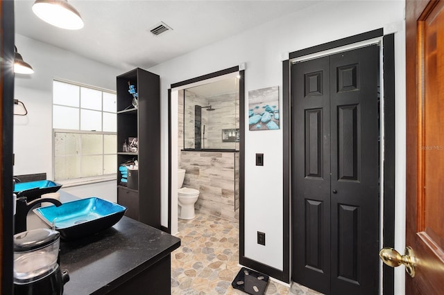 bathroom with tiled shower, vanity, and toilet