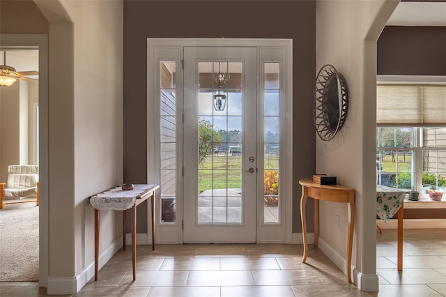 doorway to outside with arched walkways, ceiling fan, tile patterned floors, and baseboards