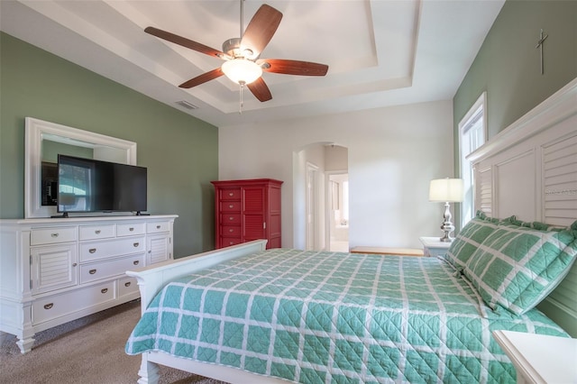 bedroom with arched walkways, carpet, a raised ceiling, visible vents, and ceiling fan