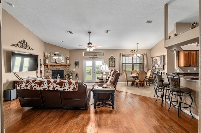 living room featuring hardwood / wood-style floors, ceiling fan with notable chandelier, vaulted ceiling, a fireplace, and a textured ceiling