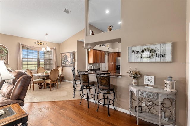 kitchen with stainless steel refrigerator with ice dispenser, kitchen peninsula, a chandelier, light hardwood / wood-style floors, and a breakfast bar area