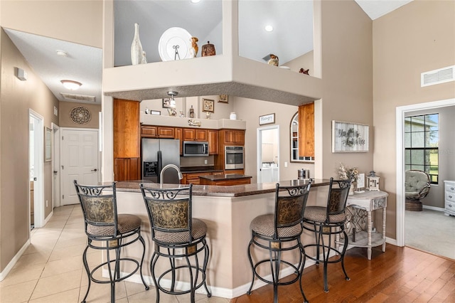 kitchen with a breakfast bar, kitchen peninsula, a high ceiling, and appliances with stainless steel finishes