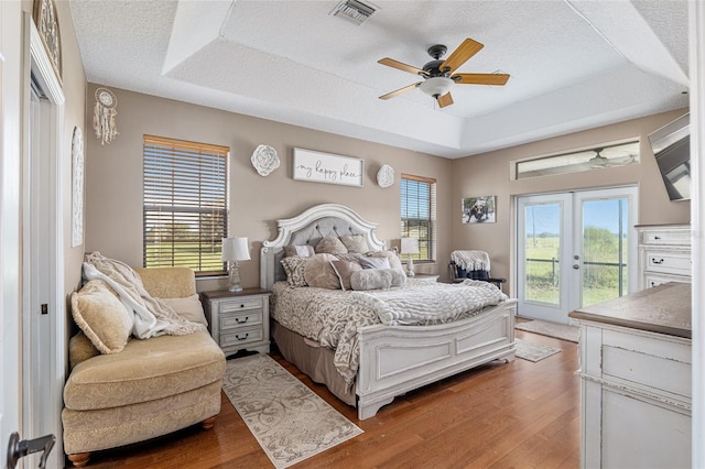 bedroom featuring french doors, access to outside, a raised ceiling, ceiling fan, and hardwood / wood-style floors