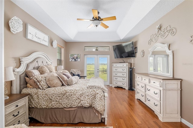 bedroom featuring access to outside, ceiling fan, light wood-type flooring, a textured ceiling, and a tray ceiling