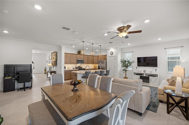 dining space with ceiling fan, crown molding, light tile patterned floors, and sink