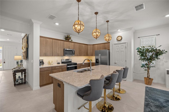 kitchen with a center island with sink, hanging light fixtures, sink, appliances with stainless steel finishes, and light stone counters