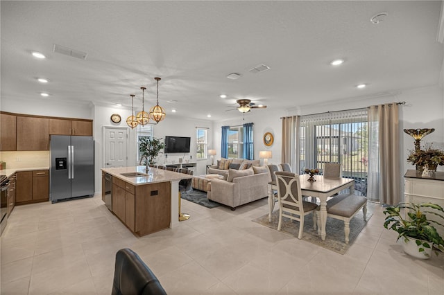 kitchen featuring appliances with stainless steel finishes, ceiling fan with notable chandelier, a kitchen island with sink, sink, and hanging light fixtures