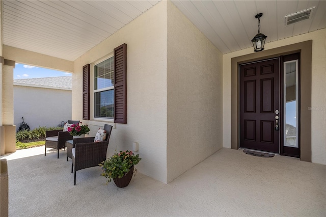 entrance to property featuring visible vents, covered porch, and stucco siding