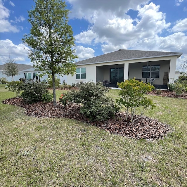 back of house with a shingled roof, stucco siding, and a yard