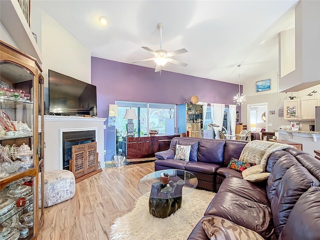 living room with ceiling fan with notable chandelier, high vaulted ceiling, and light hardwood / wood-style flooring