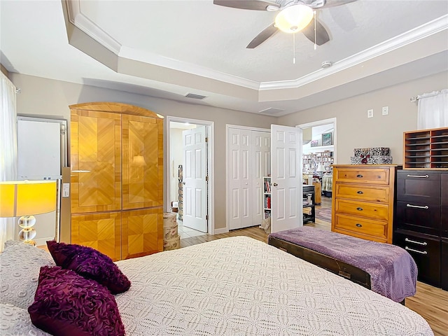 bedroom featuring light wood-type flooring, a raised ceiling, ceiling fan, and crown molding