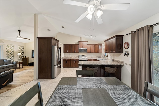 kitchen featuring lofted ceiling, kitchen peninsula, sink, light tile patterned flooring, and stainless steel appliances