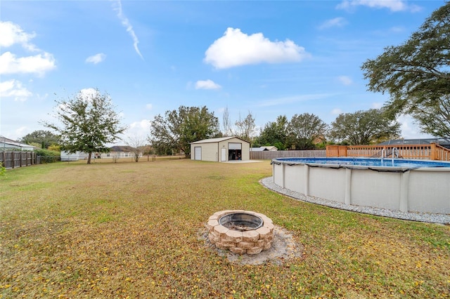 view of yard with a garage, a fenced in pool, an outbuilding, and a fire pit