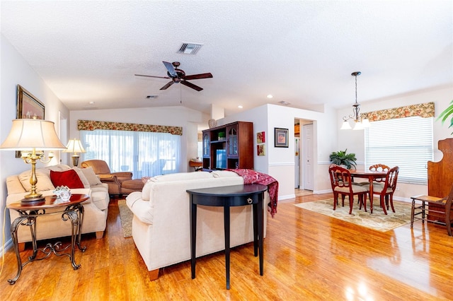 living room featuring ceiling fan with notable chandelier, light wood-type flooring, a textured ceiling, and vaulted ceiling