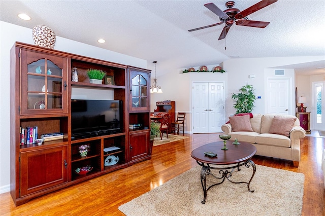 living room with lofted ceiling, light hardwood / wood-style flooring, ceiling fan with notable chandelier, and a textured ceiling