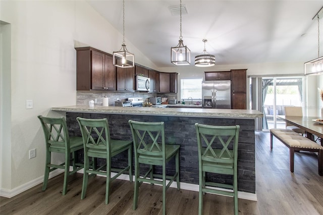 kitchen featuring pendant lighting, vaulted ceiling, dark brown cabinets, kitchen peninsula, and stainless steel appliances