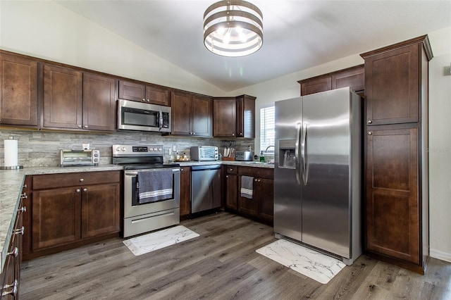 kitchen with tasteful backsplash, light stone countertops, stainless steel appliances, and lofted ceiling