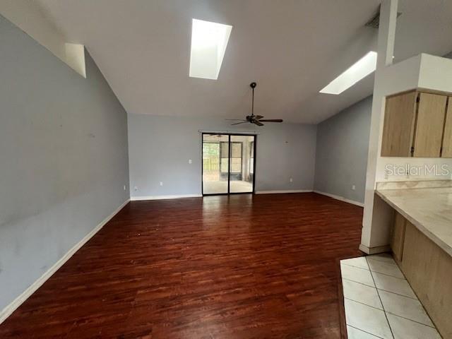 unfurnished living room with a skylight, ceiling fan, dark hardwood / wood-style flooring, and high vaulted ceiling