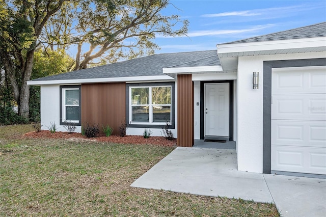 entrance to property featuring an attached garage, a lawn, and roof with shingles