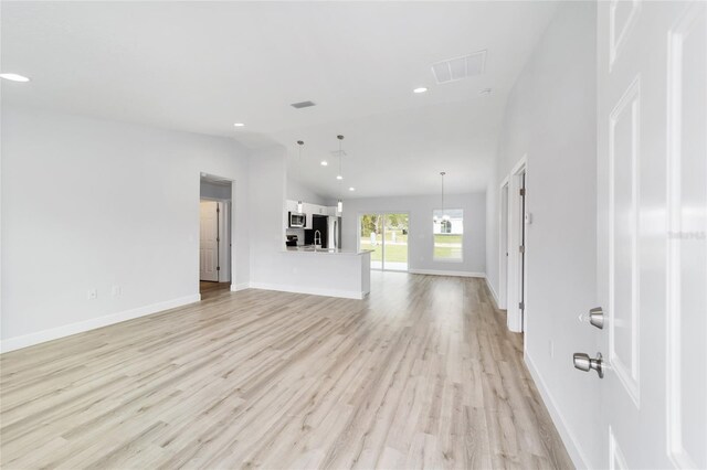 unfurnished living room with baseboards, visible vents, vaulted ceiling, light wood-style floors, and recessed lighting