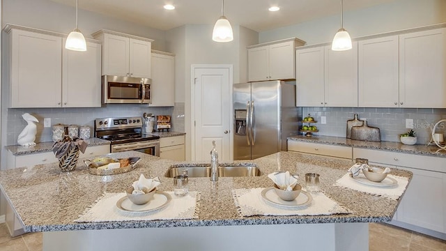 kitchen with decorative light fixtures, stainless steel appliances, and a kitchen island with sink