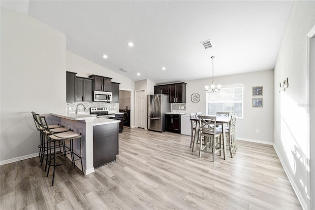 kitchen featuring a kitchen bar, appliances with stainless steel finishes, kitchen peninsula, and vaulted ceiling