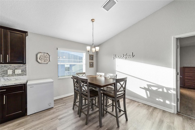 dining area featuring vaulted ceiling, an inviting chandelier, and light hardwood / wood-style floors