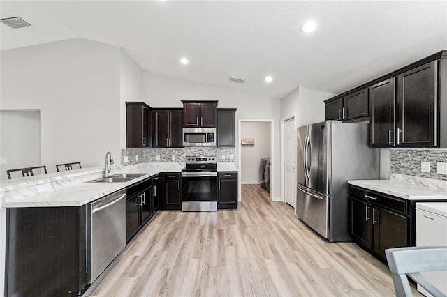 kitchen featuring vaulted ceiling, decorative backsplash, sink, a breakfast bar area, and stainless steel appliances