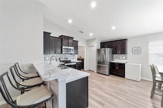 kitchen featuring a kitchen bar, backsplash, appliances with stainless steel finishes, and vaulted ceiling