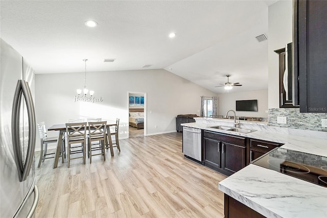 kitchen featuring vaulted ceiling, sink, hanging light fixtures, stainless steel appliances, and ceiling fan with notable chandelier