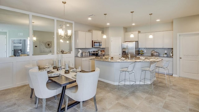 kitchen featuring decorative backsplash, stainless steel appliances, a kitchen island with sink, decorative light fixtures, and white cabinetry