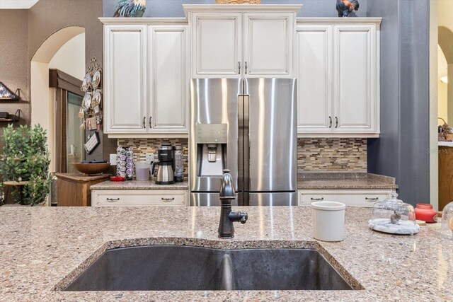 kitchen with white cabinets, stainless steel fridge, light stone counters, and tasteful backsplash