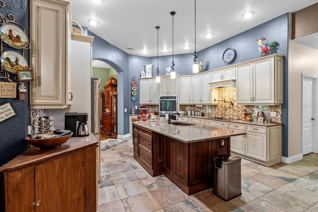 kitchen with light stone counters, sink, hanging light fixtures, lofted ceiling, and an island with sink