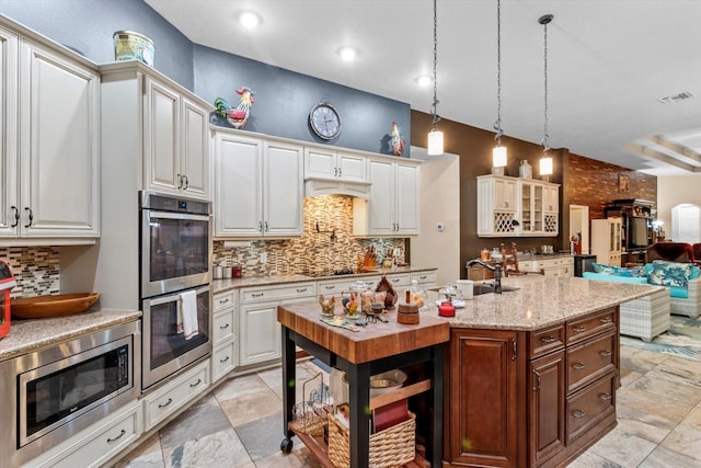 kitchen with pendant lighting, a kitchen island with sink, sink, white cabinetry, and stainless steel appliances