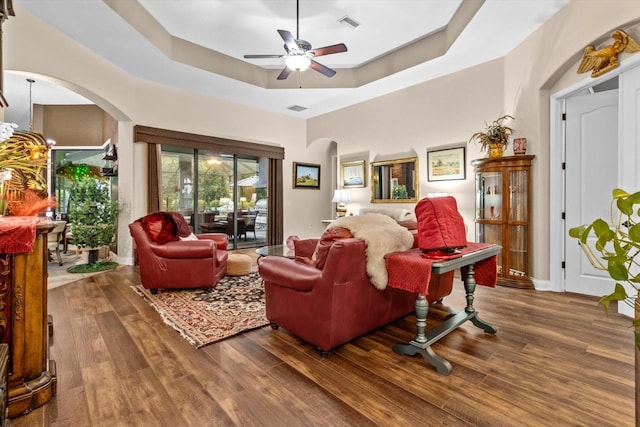 living room with hardwood / wood-style floors, a raised ceiling, and ceiling fan