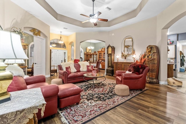 living room featuring ceiling fan with notable chandelier, a raised ceiling, and dark wood-type flooring