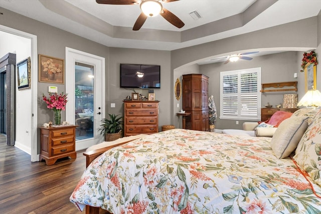 bedroom featuring a raised ceiling, access to exterior, ceiling fan, and dark wood-type flooring